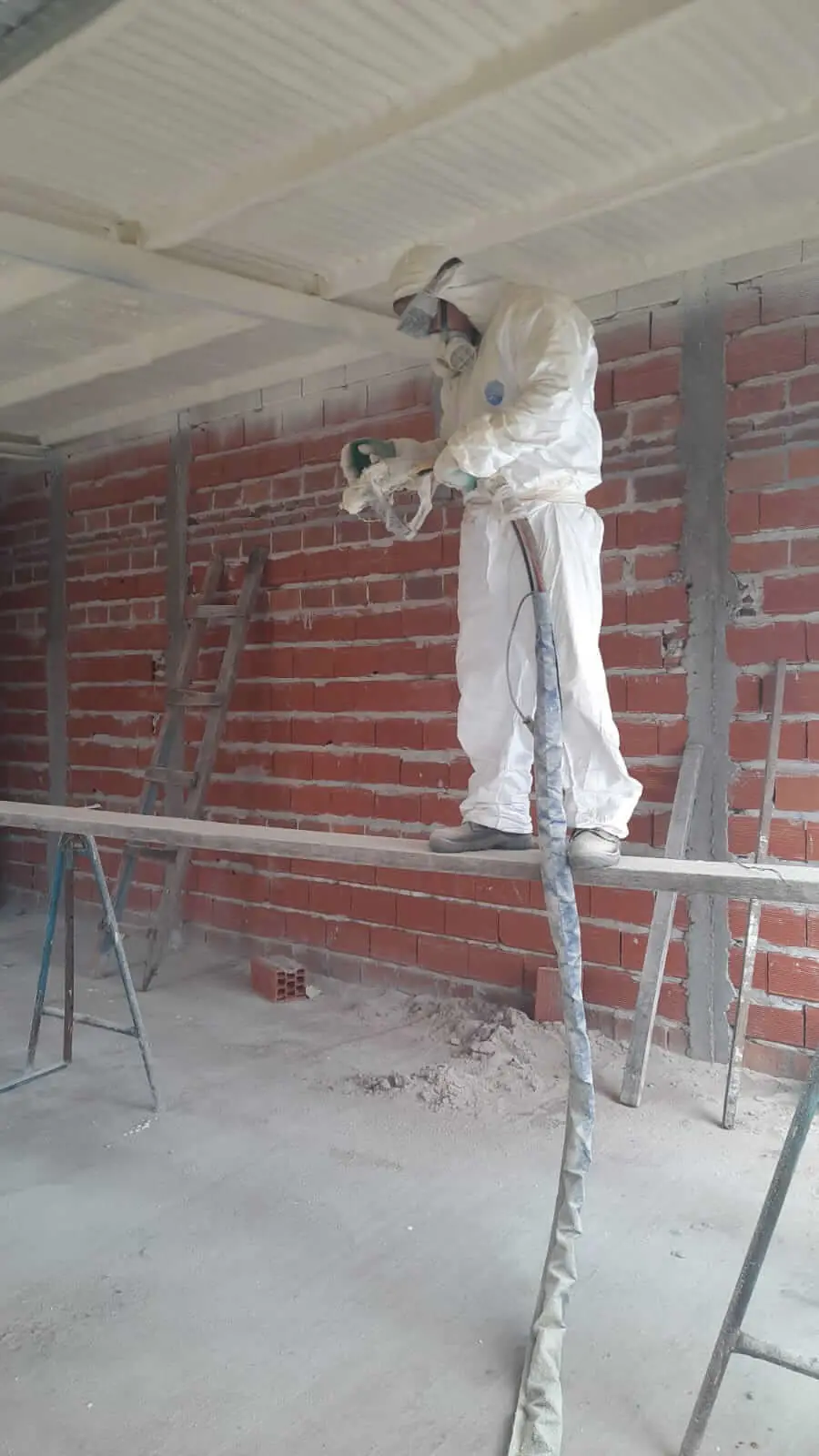 Operario proyectando poliuretano expandido sobre el cielorraso de viguetas de una obra en construcción.