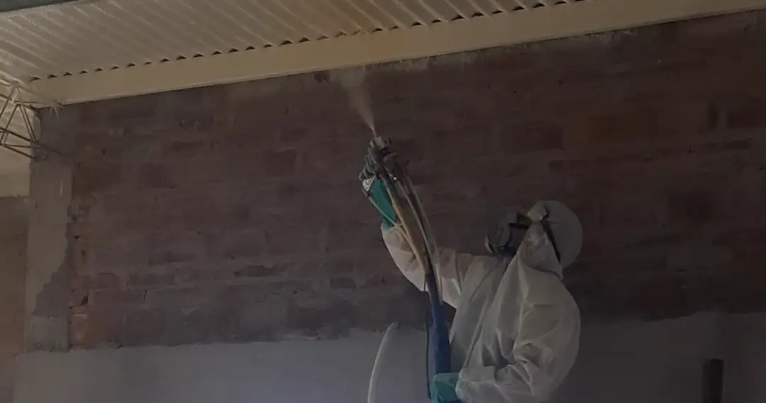 Operario de FEYSA proyectando poliuretano expandido sobre el encuentro de un muro de ladrillo con la cubierta de chapa.